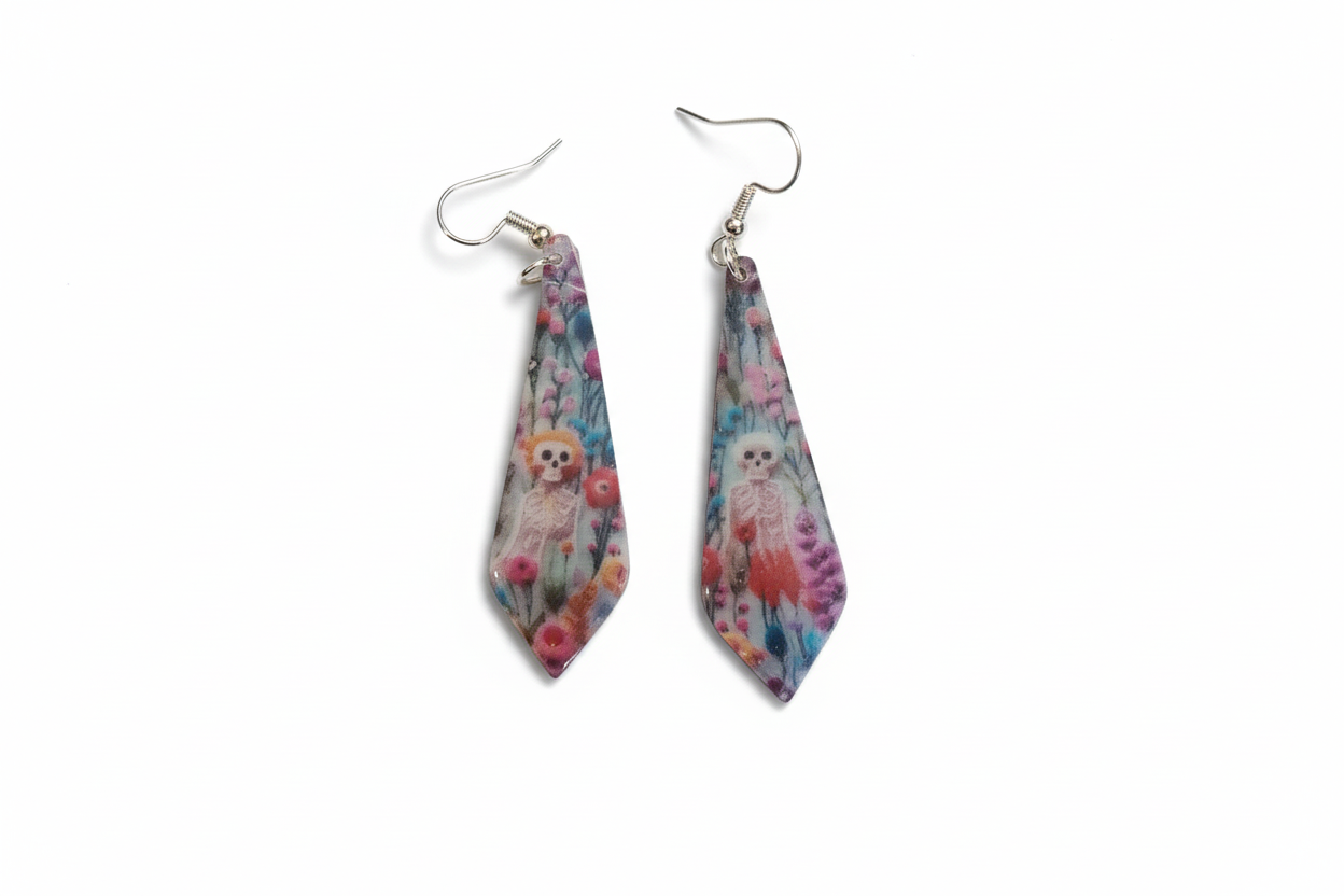 This image displays a pair of striking earrings featuring an intricate embroidered design. The earrings are adorned with a vibrant mix of floral patterns and skeletal motifs, presented on a wooden surface.